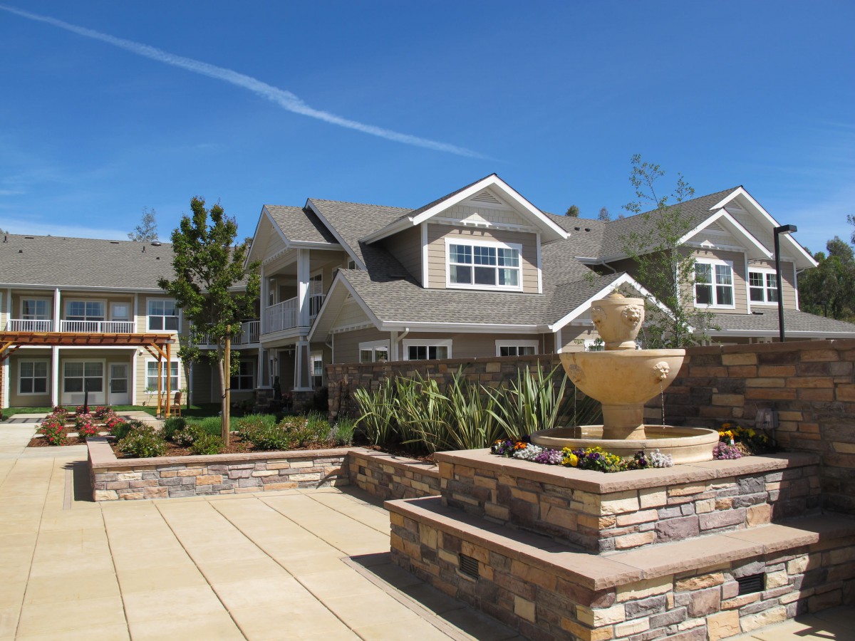 A modern residential building with a landscaped courtyard and fountain under a clear blue sky.