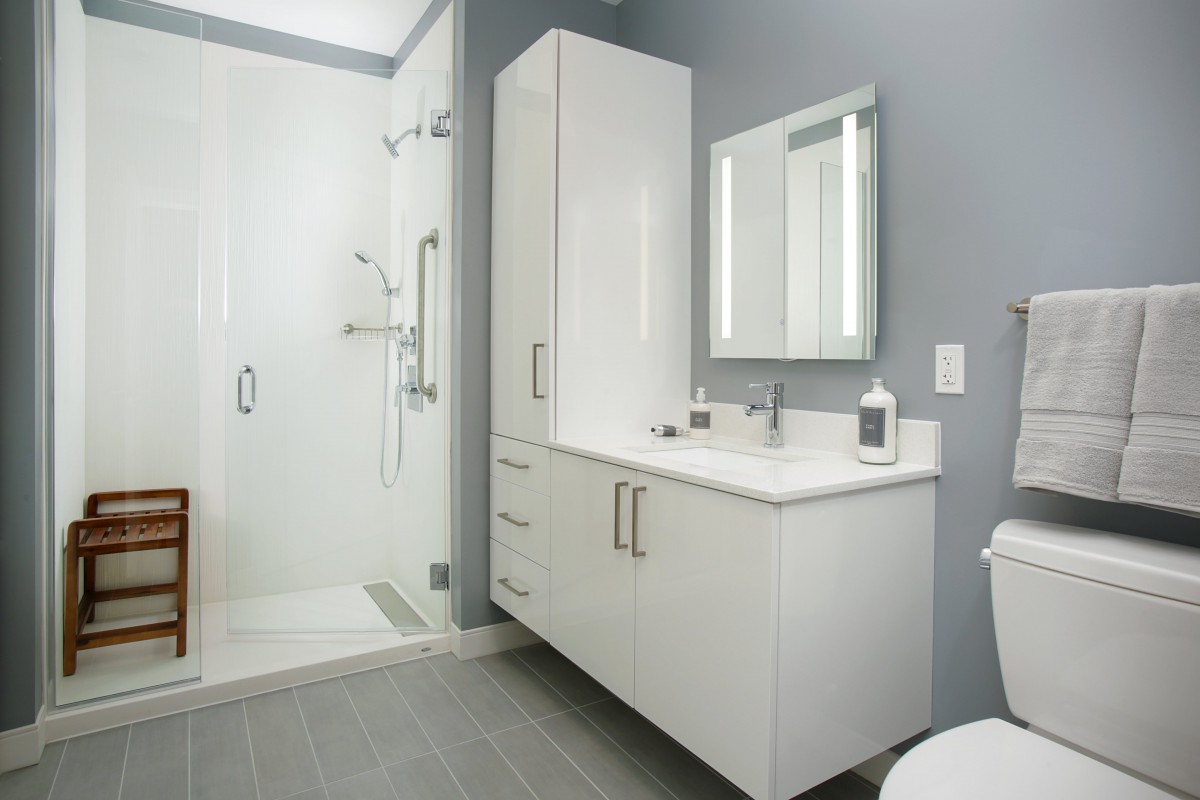 A modern, minimalist bathroom featuring a shower, sink, and white cabinets against grey walls.