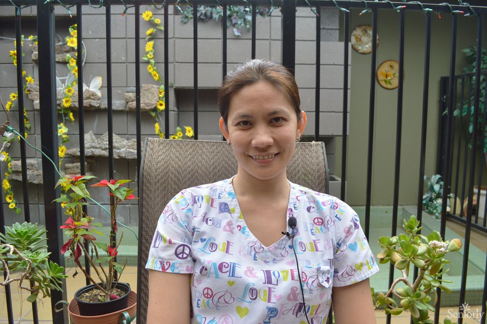 A woman smiling while sitting outdoors in a garden setting.
