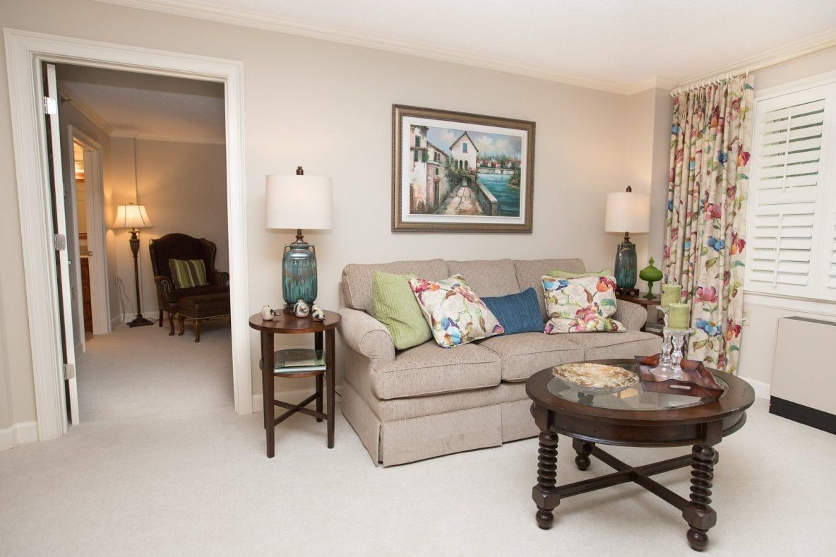 A cozy living room featuring a sofa with colorful pillows, framed artwork, and elegant lamps on side tables.