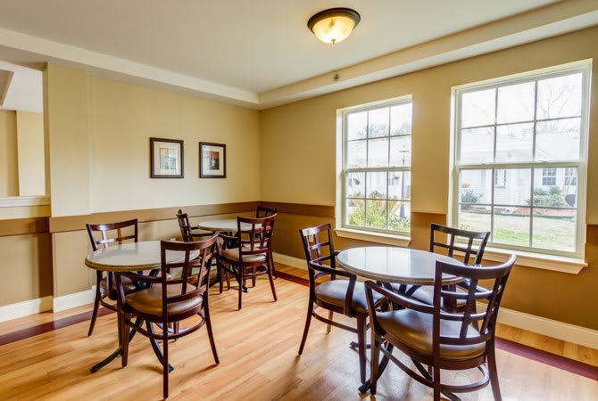 A cozy cafe with several tables and chairs, featuring wooden flooring and natural light from large windows.