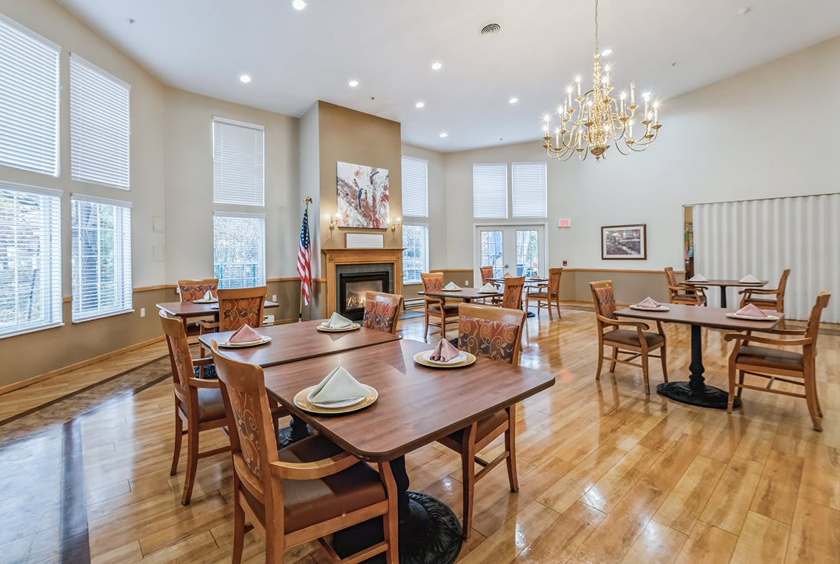 A spacious dining room with neatly arranged tables and chairs, illuminated by a chandelier.