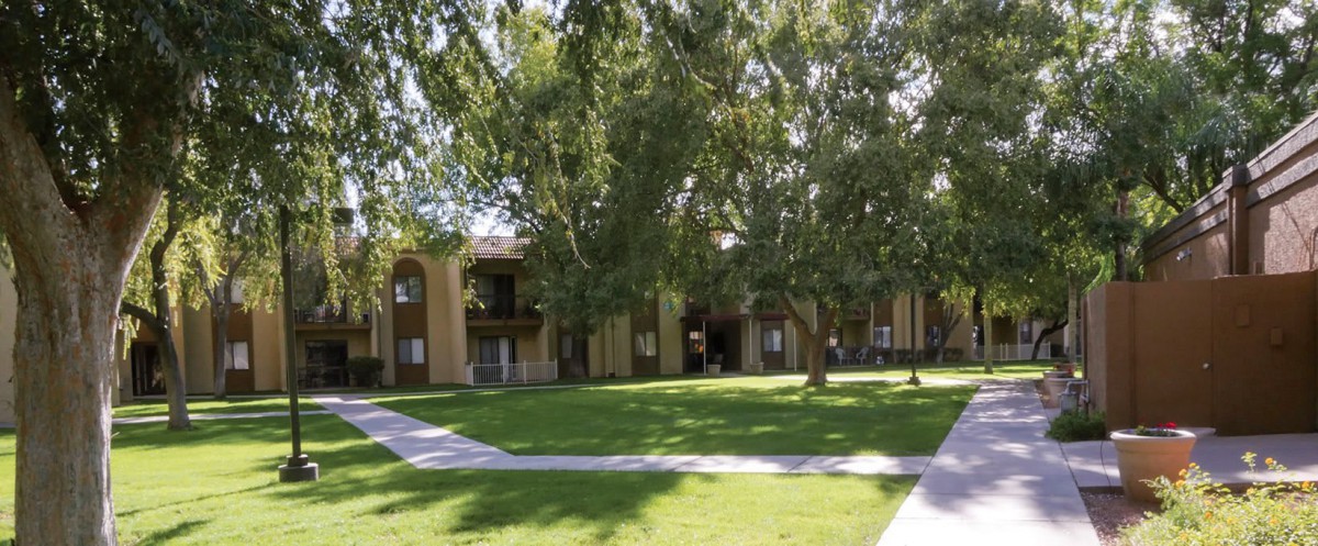 An outdoor view of an apartment complex with a well-maintained lawn and trees.