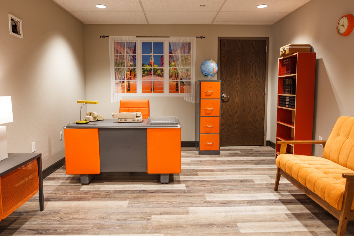 A modern office space featuring vibrant orange furniture, a globe on a filing cabinet, and a stylish wall art piece.