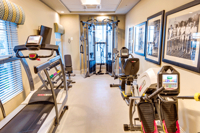 A small, well-equipped gym room with various exercise machines and weights.