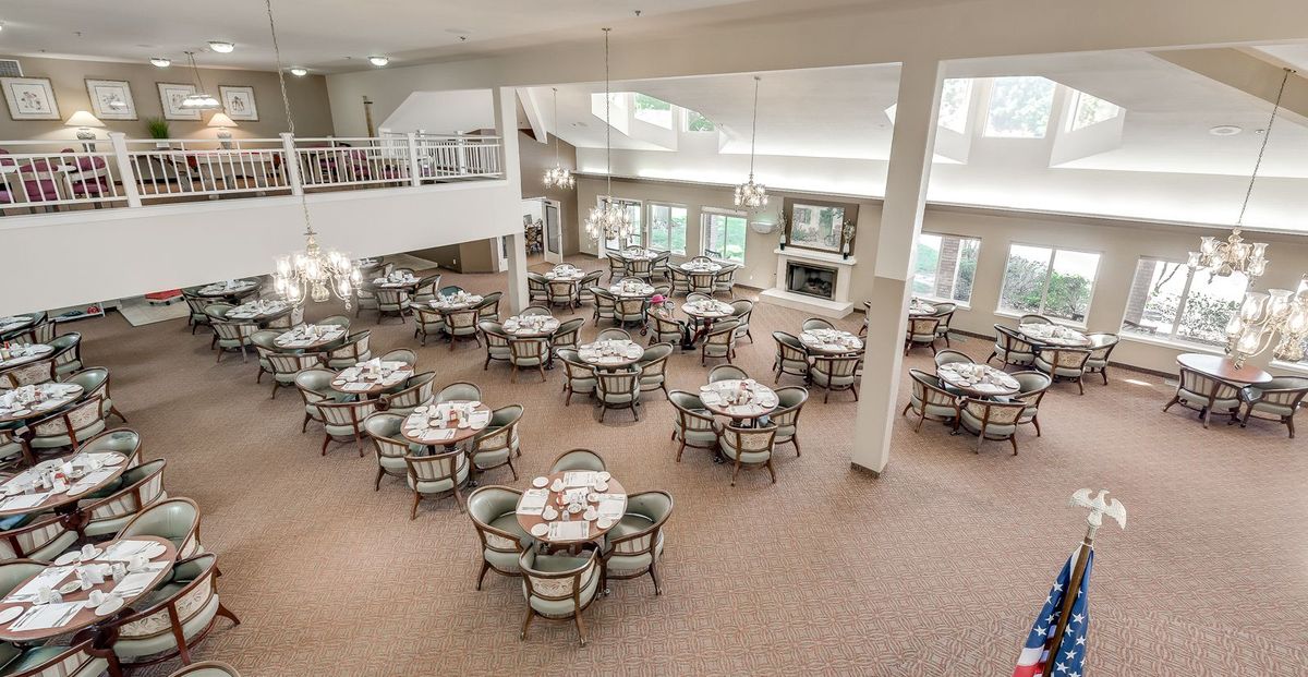 A spacious and elegantly arranged dining room with multiple round tables set for service.