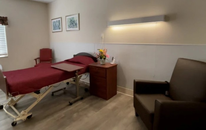 A tidy hospital room featuring a bed, bedside table, and comfortable chair.