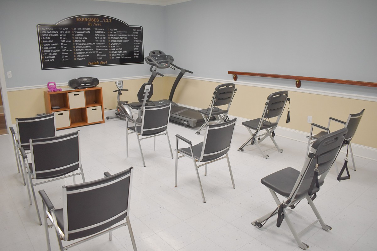 An indoor classroom setup with chairs arranged in a semi-circle and exercise equipment in the background.