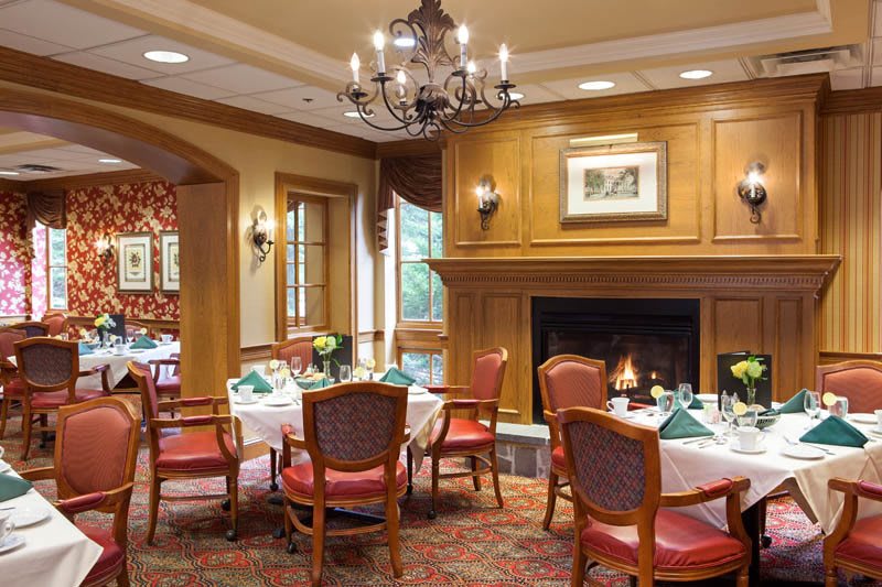Elegant dining area with a fireplace and chandelier, featuring classic wooden decor and neatly set tables.