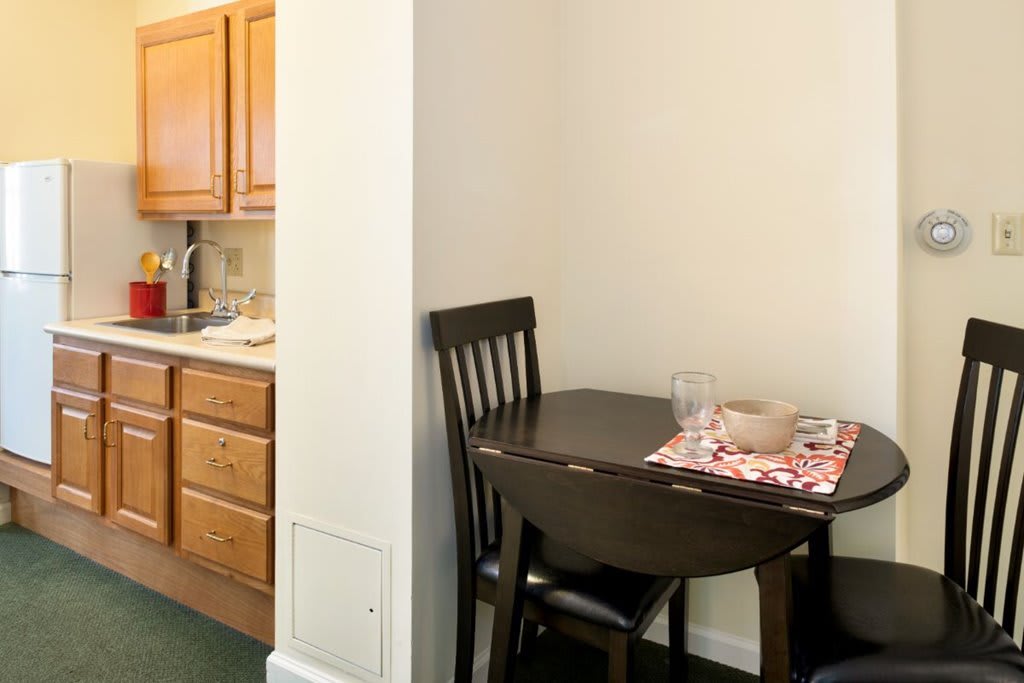 A cozy dining nook adjacent to a small kitchen area, featuring a wooden table set for two.