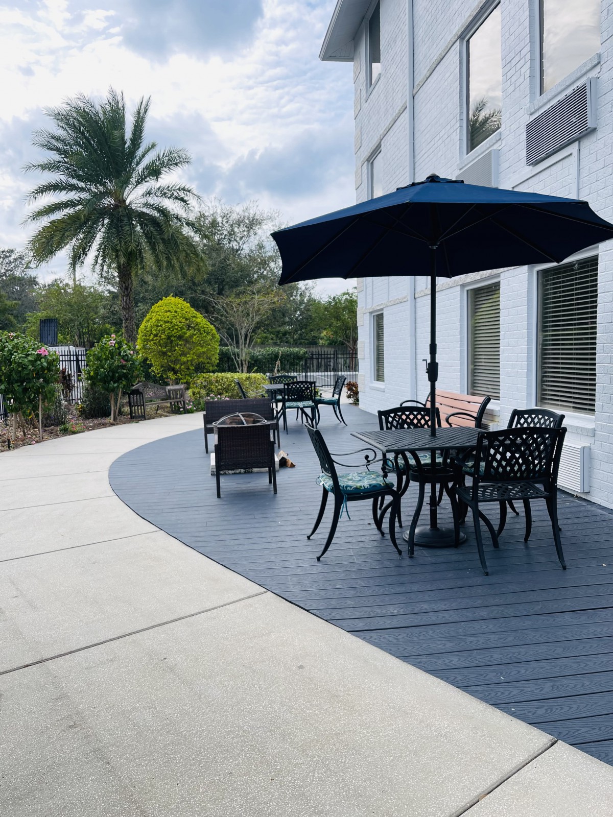 A serene outdoor patio area with a black umbrella, table, and chairs surrounded by lush landscaping.