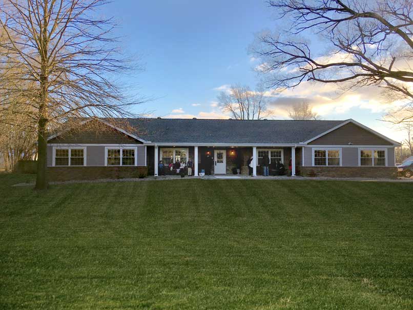 A suburban house with a large lawn and a porch, surrounded by bare trees under a clear sky.