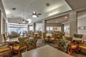 Spacious dining area with multiple tables and chairs, featuring ceiling fans and ample natural lighting.