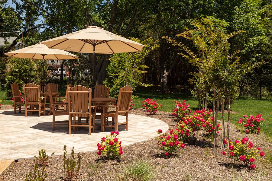 A garden patio area featuring wooden chairs and a table under an umbrella, surrounded by vibrant flowers.