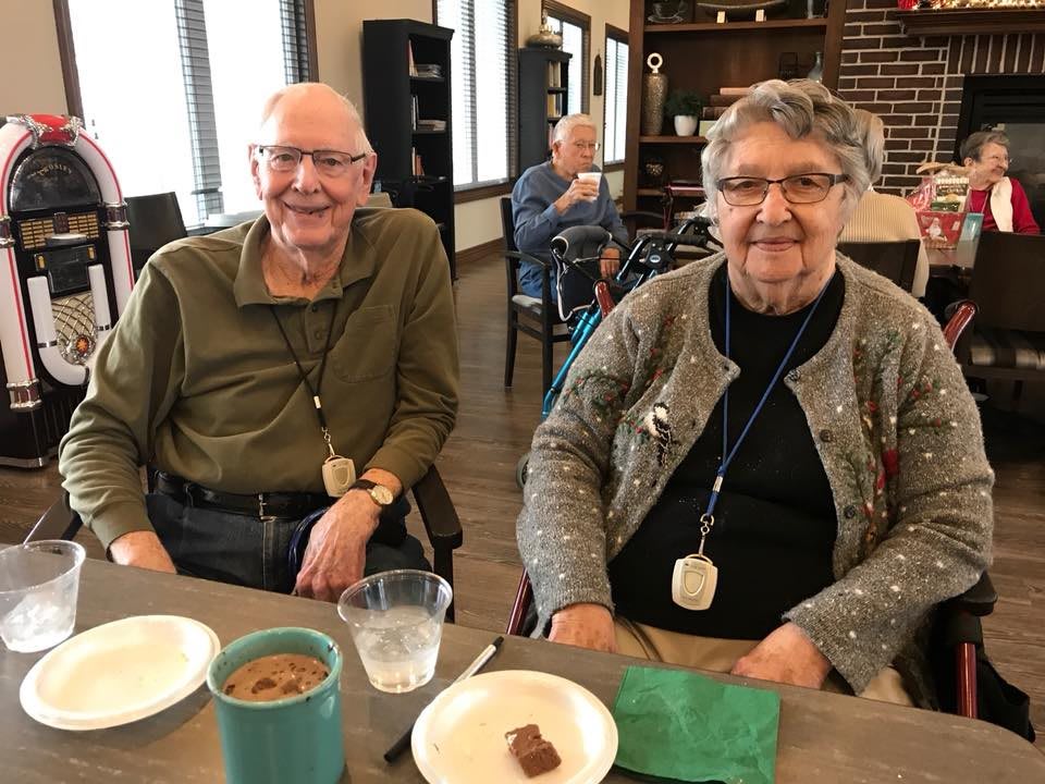 An elderly couple enjoying a meal together indoors, smiling at the camera.