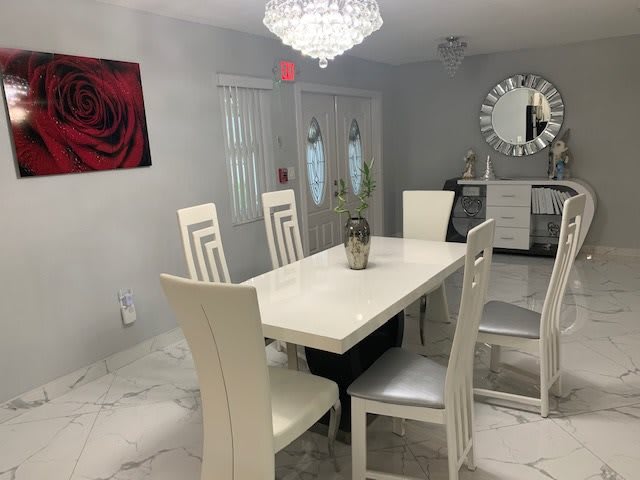 A modern dining room featuring white furniture, a chandelier, and rose-themed artwork.