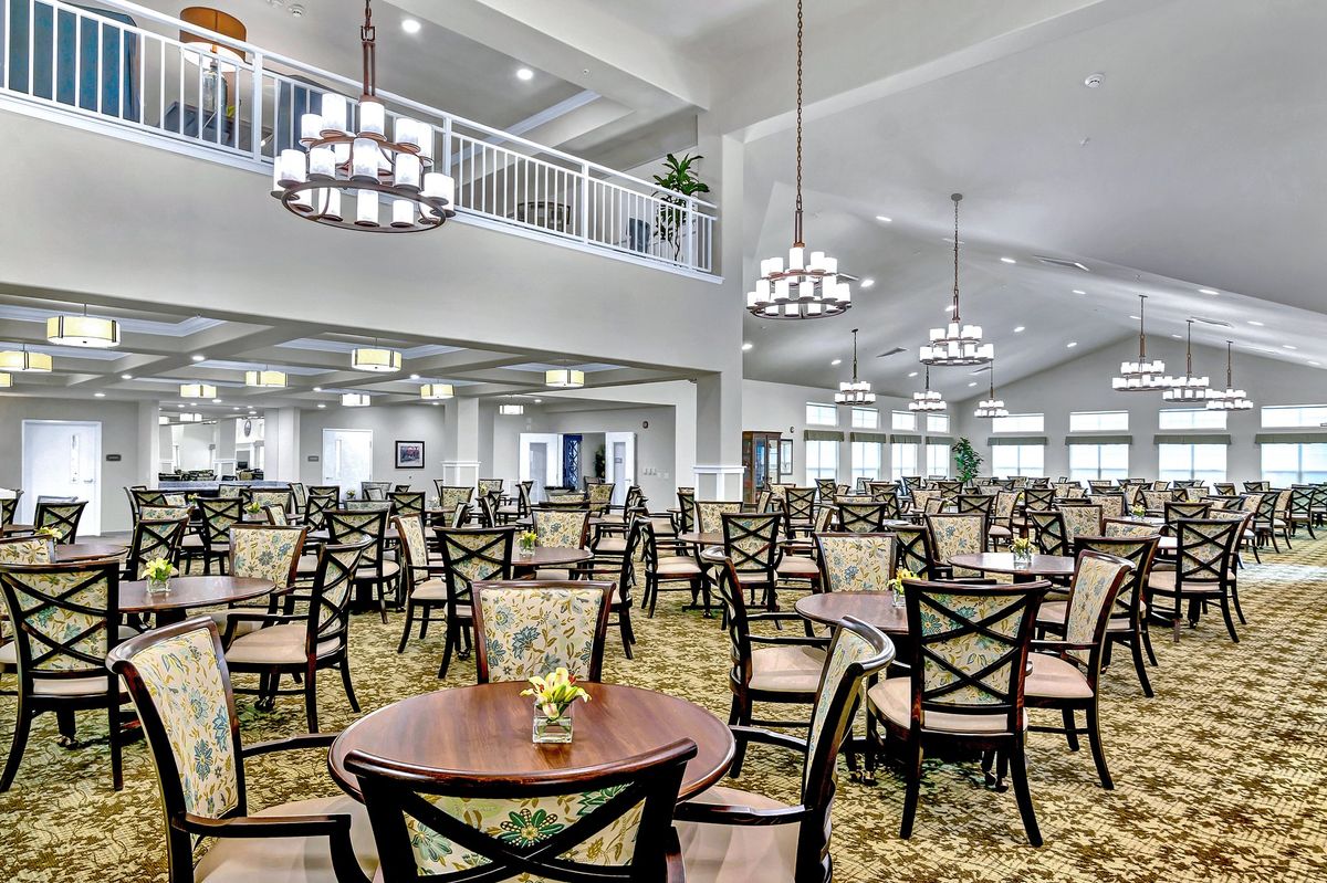 A spacious and elegantly designed dining hall featuring numerous tables and chairs under grand chandeliers.