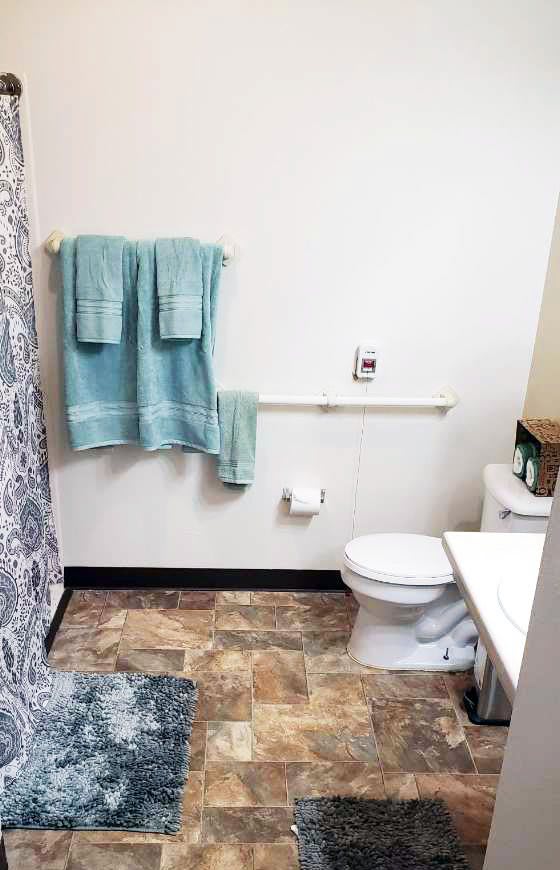 A clean and organized bathroom with teal towels, a patterned shower curtain, and a tiled floor.