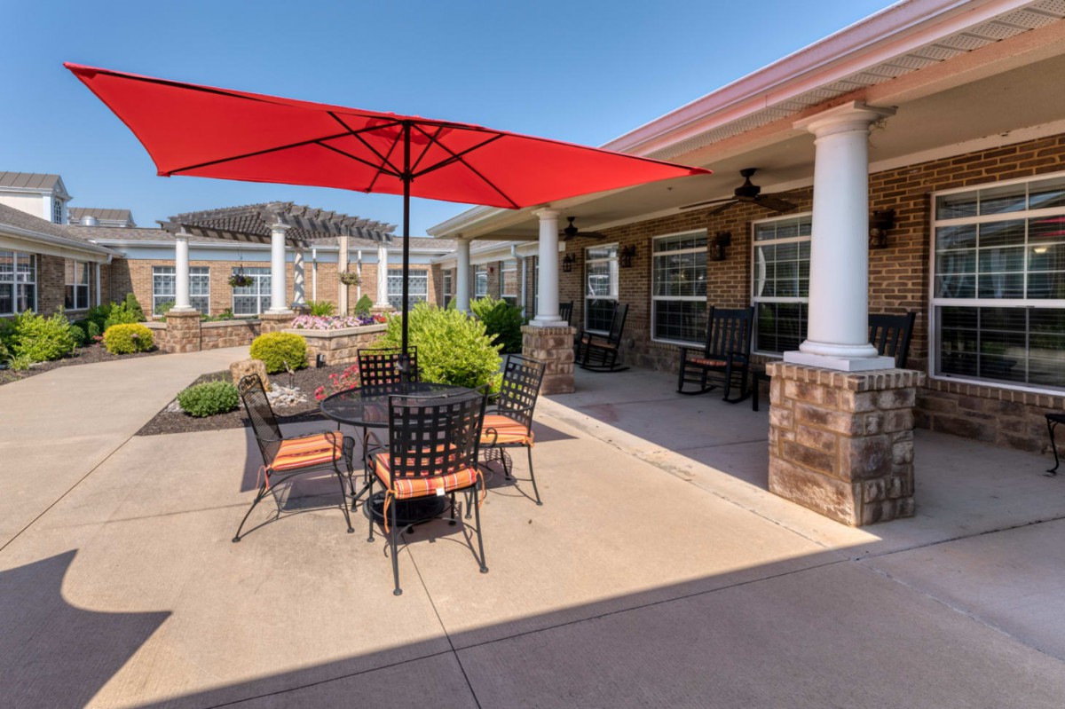 A sunny outdoor patio with a red umbrella and seating area.