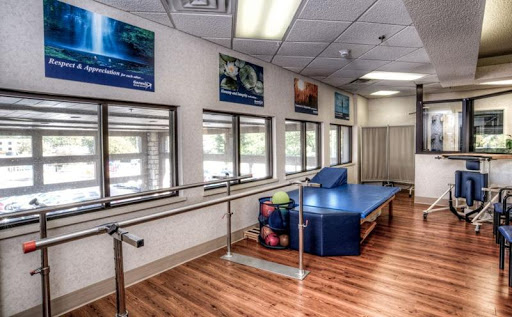 A spacious physical therapy room equipped with a barre, colorful exercise balls, and large windows allowing natural light.
