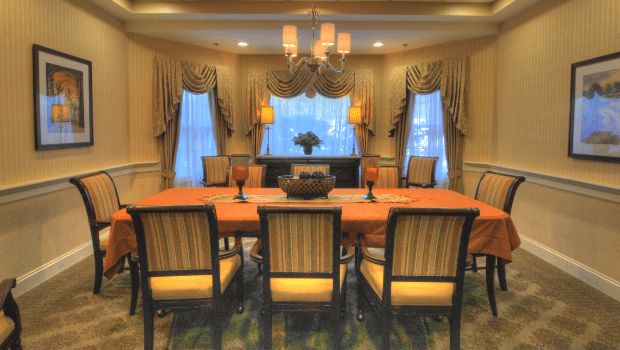 An elegantly decorated dining room with a large table, cushioned chairs, and a central chandelier.