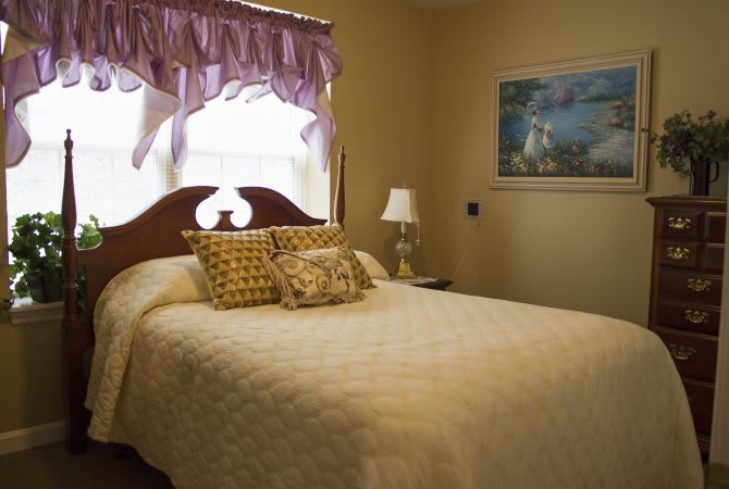 A cozy bedroom featuring a neatly made bed with decorative pillows, a bedside lamp, and a painting on the wall.