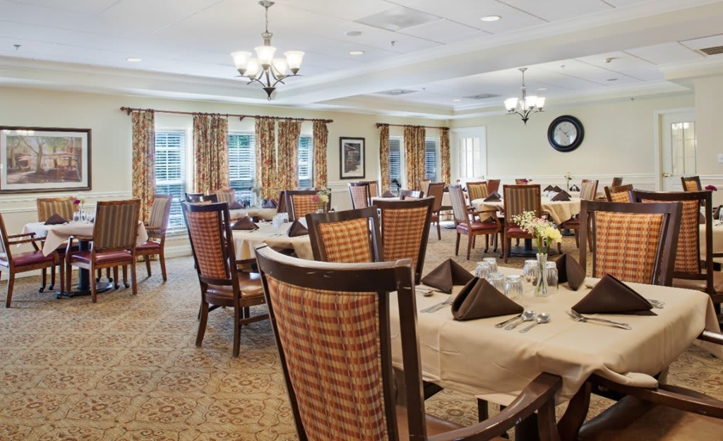 A well-decorated dining room with neatly arranged tables and chairs, set under elegant chandeliers.