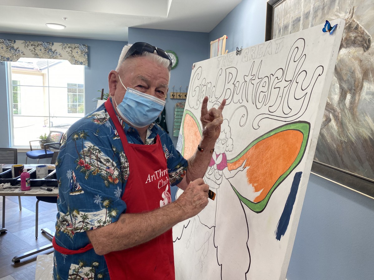 Man wearing a mask paints a colorful canvas indoors.