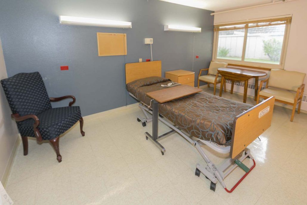 A well-lit hospital room featuring a bed, chair, and table.