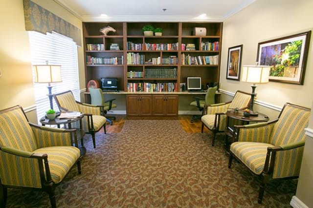 A cozy library room with bookshelves, comfortable seating, and a computer desk.