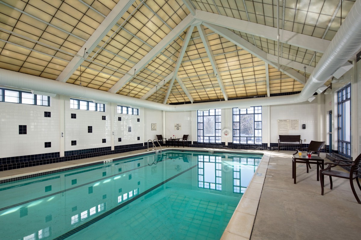 A spacious indoor swimming pool with a high, grid-patterned ceiling and large windows allowing natural light to flood the area.