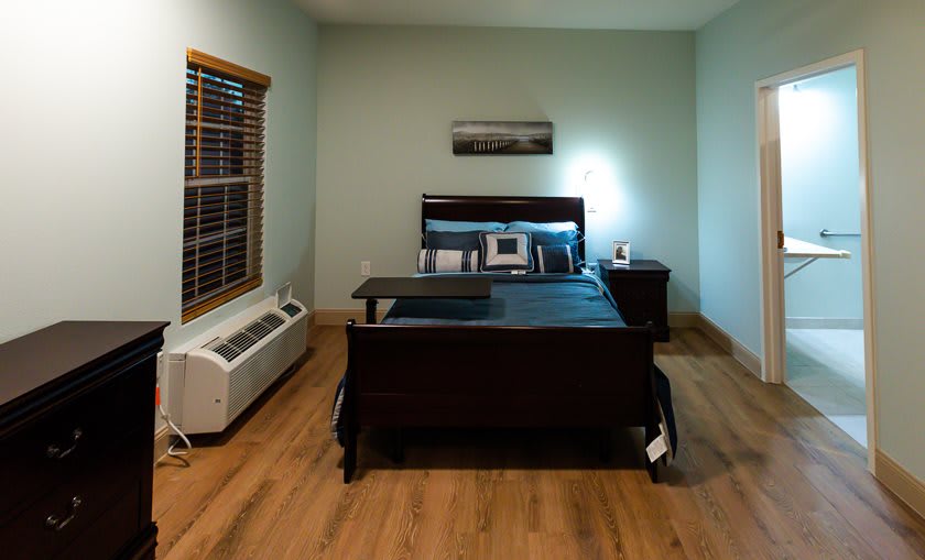 A cozy bedroom with a dark wooden bed and nightstand, featuring an air conditioner and hardwood flooring.