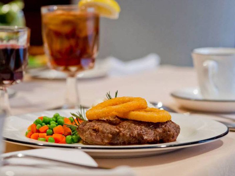 A delicious steak topped with grilled pineapple, accompanied by a side of peas and carrots, served with a glass of iced tea.