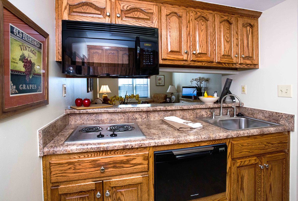 A cozy kitchen featuring wooden cabinets, a stove top, microwave, and a sink on a granite countertop.