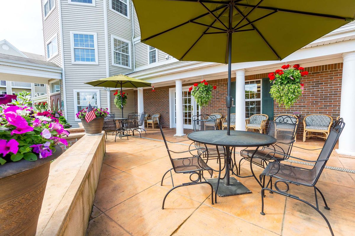 A cozy patio with tables, chairs, and umbrellas, surrounded by flowers and adjacent to a building.