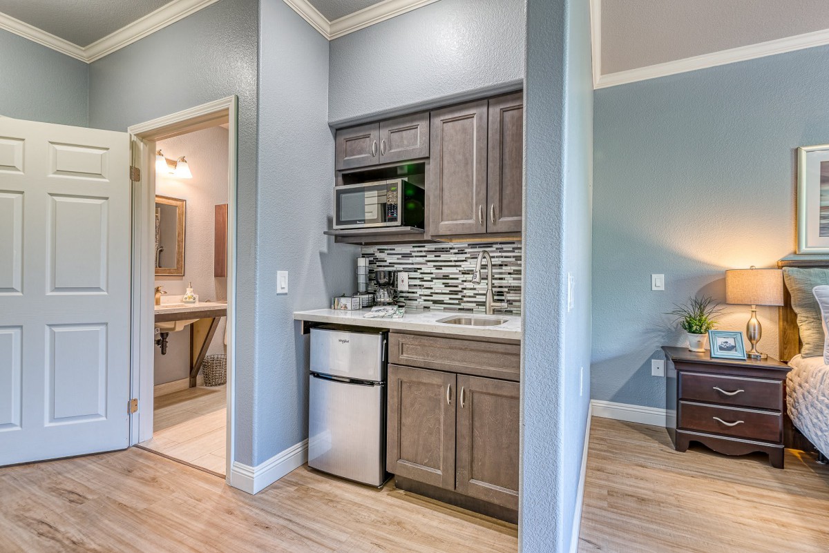 A modern kitchenette featuring a small fridge, microwave, and stylish cabinetry with a tiled backsplash.