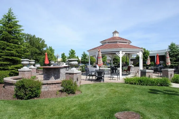 A beautiful outdoor space featuring a gazebo with seating, surrounded by well-maintained landscaping on a sunny day.