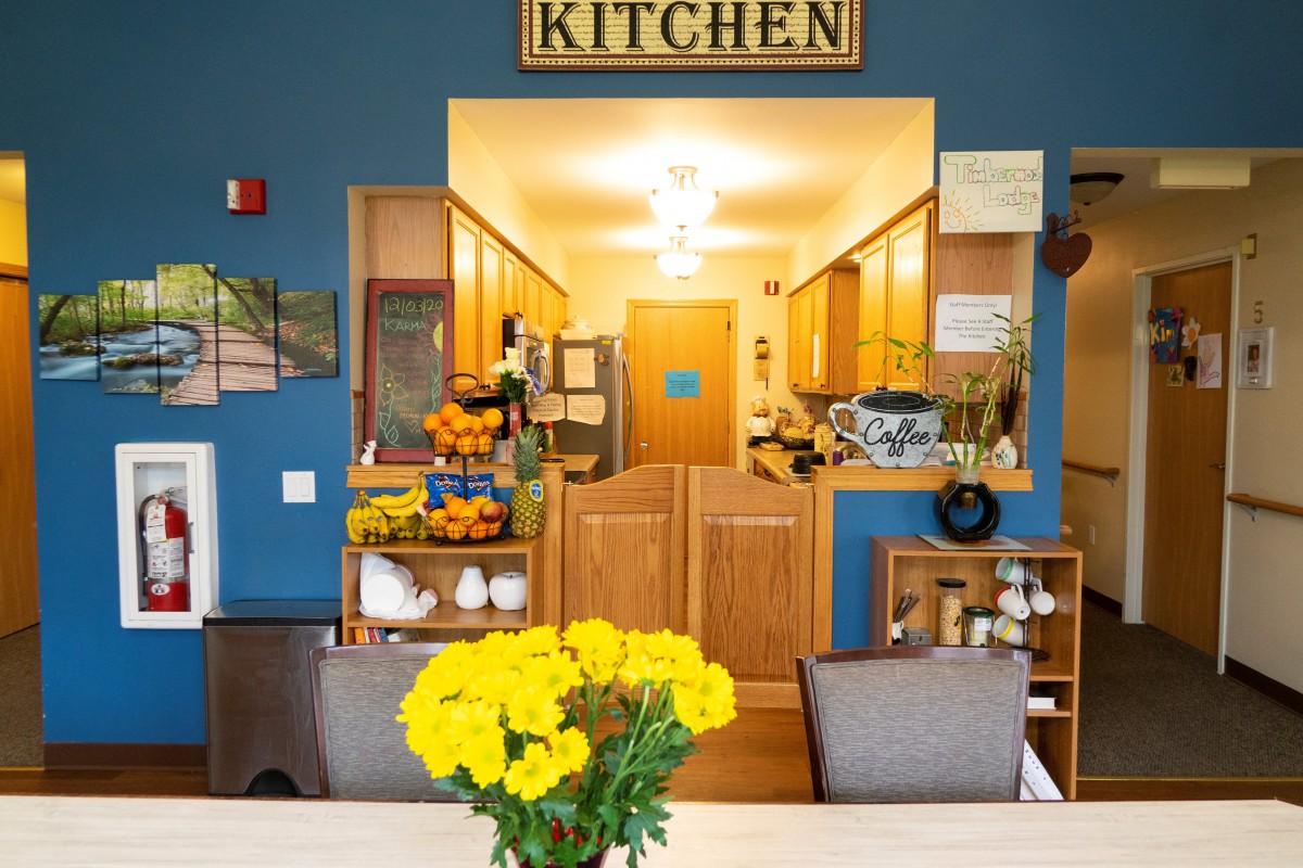 A cozy kitchen interior with a dining area, featuring bright yellow flowers on the table and warm wooden cabinetry.