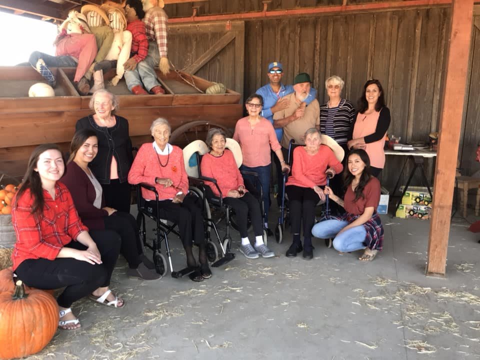 A group of people posing outside a barn, with some seated in wheelchairs.