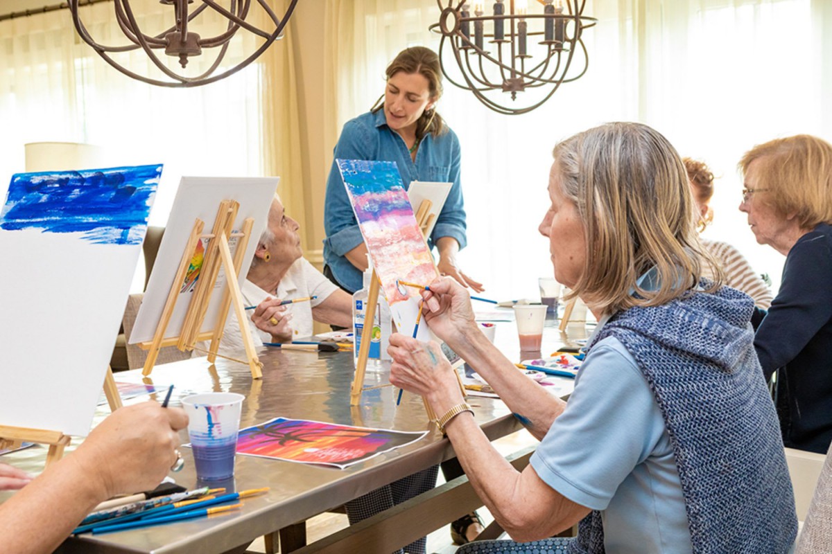 A group of people participating in an art class, painting on canvases set on easels in a well-lit room.