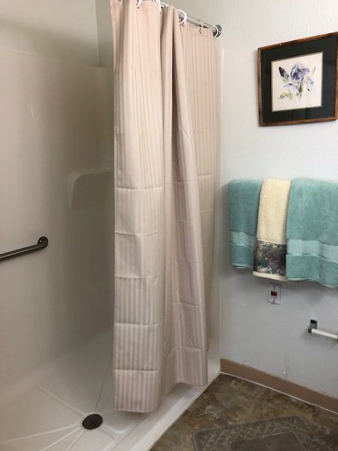 A bathroom with a shower, light-colored shower curtain, teal and white towels, and wall art.