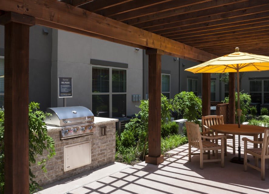 A sunny outdoor patio with a barbecue grill and dining area under a wooden pergola.