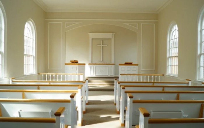 Interior view of a serene chapel with wooden pews and a central altar featuring a cross.