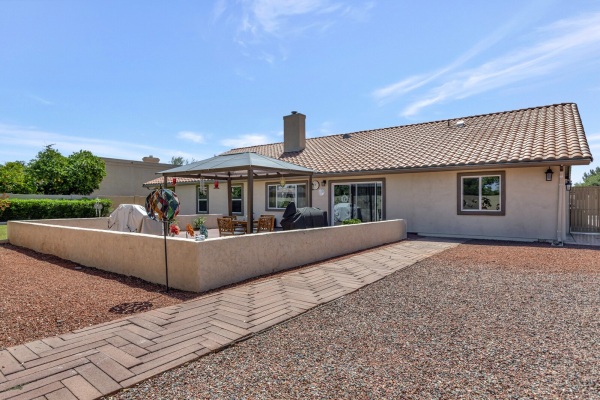 A view of a backyard with a patio area and gravel landscaping under a clear blue sky.