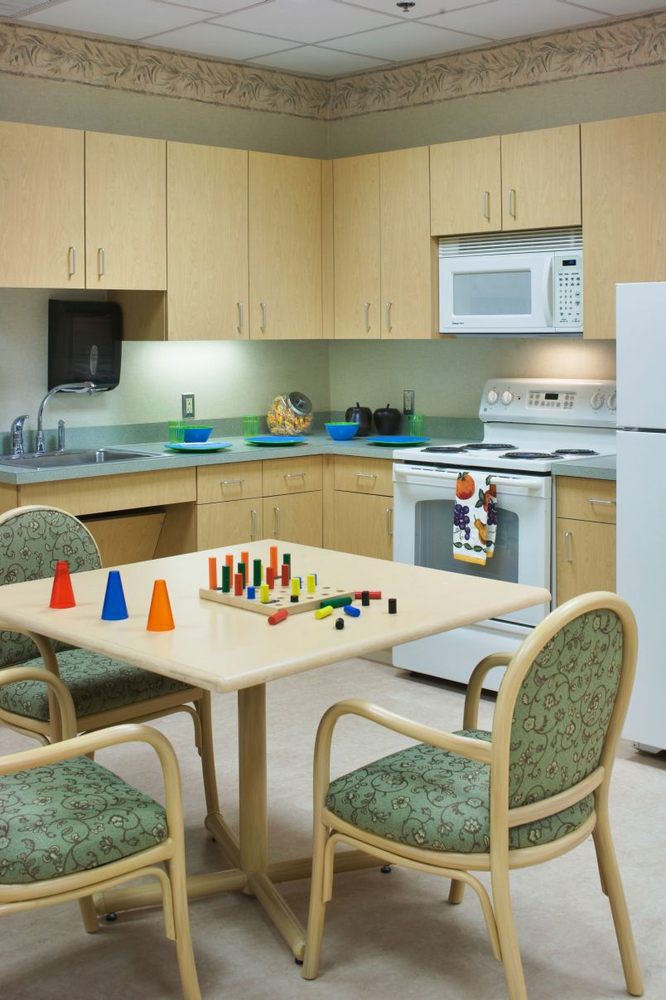 A kitchen setup with wooden cabinetry, basic appliances, and a table with chairs featuring colorful toys.