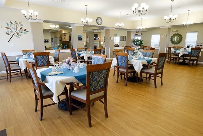 A well-lit dining room with neatly arranged tables and chairs, featuring elegant chandeliers and a wooden floor.