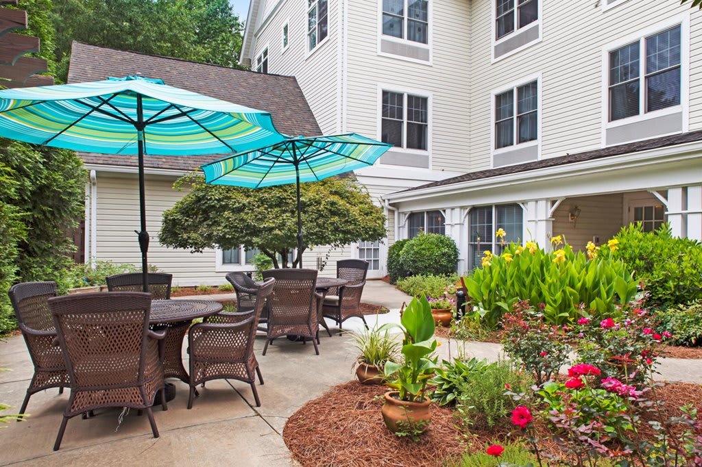A cozy outdoor patio area with tables, chairs, and colorful umbrellas surrounded by a lush garden.