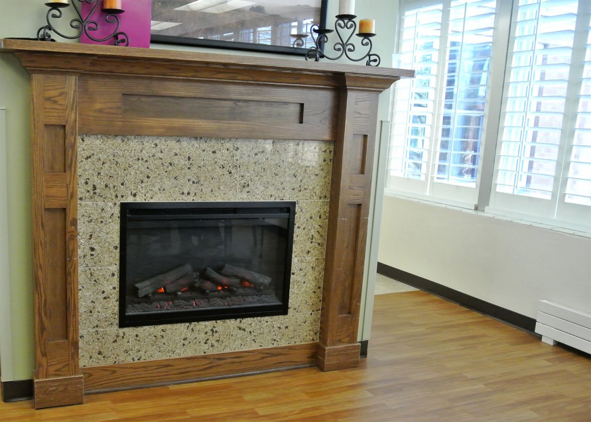 A cozy living room with a modern fireplace and wooden mantel, decorated with candles, next to a bright window.
