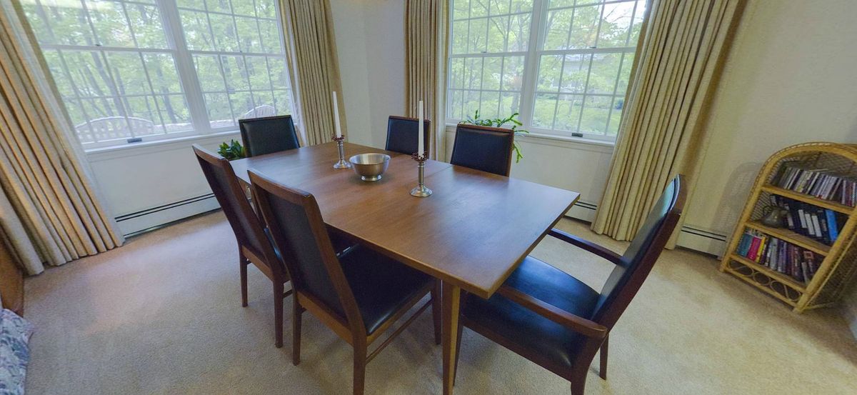 A modern dining room with a wooden table, six chairs, and candles by the window.