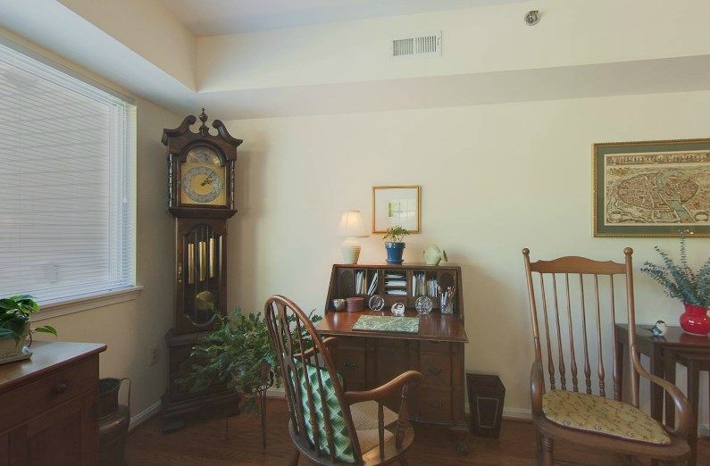 A cozy study room with a grandfather clock, wooden desk, and rocking chair.